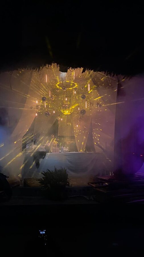 Festival stage canopy: mirror balls and filament bulbs under a thatched roof, warm light